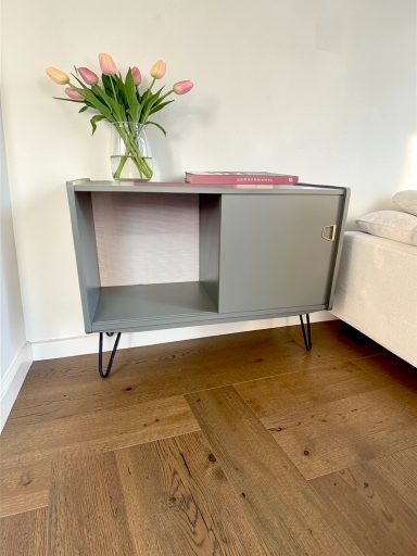 Mid-Century Schrank „Olivgrün-Modern“ Grauer Sideboard mit offenen und geschlossenen Fächern, Blumenstrauß dahinter.