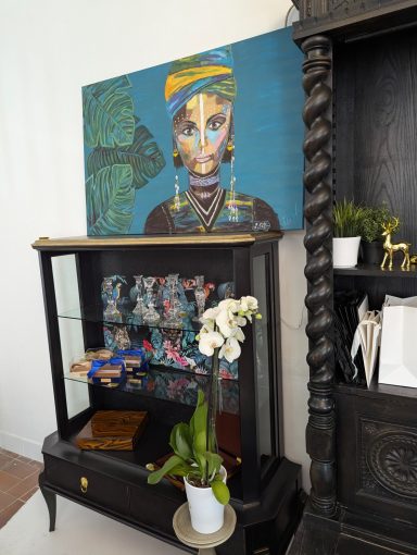 "Tropic Noir" – Ein Unikat Moderne Wandkunst mit Porträt einer Frau, schwarzer Möbelkommode mit Pflanzen und Deko.